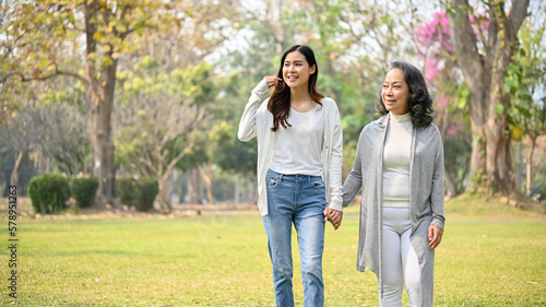 Lovely Asian female grandchild holds hands with her grandmother while strolling in the park