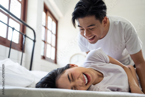 Asian attractive man tickles his girlfriend while lying down on bed. 