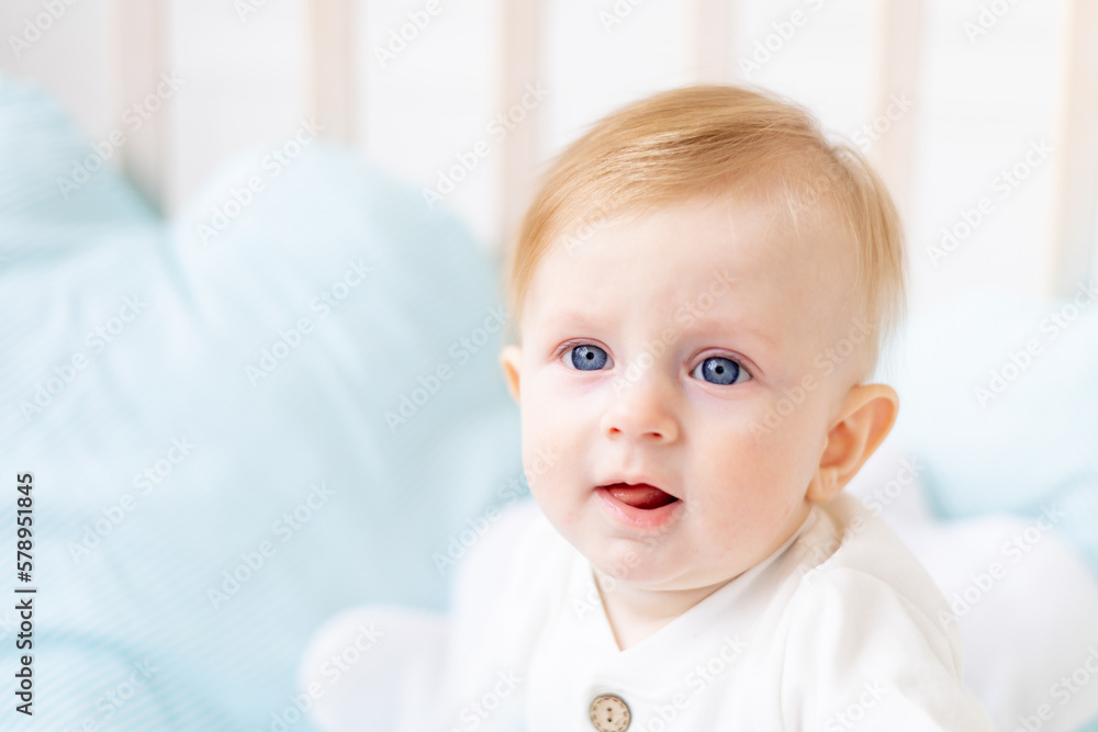 close-up portrait of a baby 6 months old, a blond boy with blue eyes in a crib in a bright bedroom in a white cotton bodysuit, the concept of children's goods