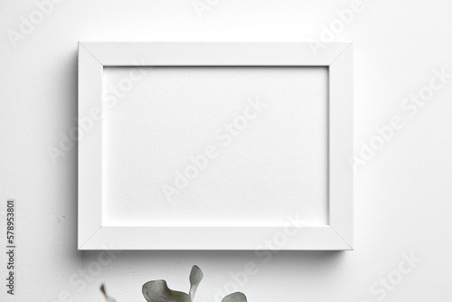 Photo frame mockup hanging on white concrete wall and bouquet of pink roses with eucalyptus leaves. Blank picture frame, interior decor