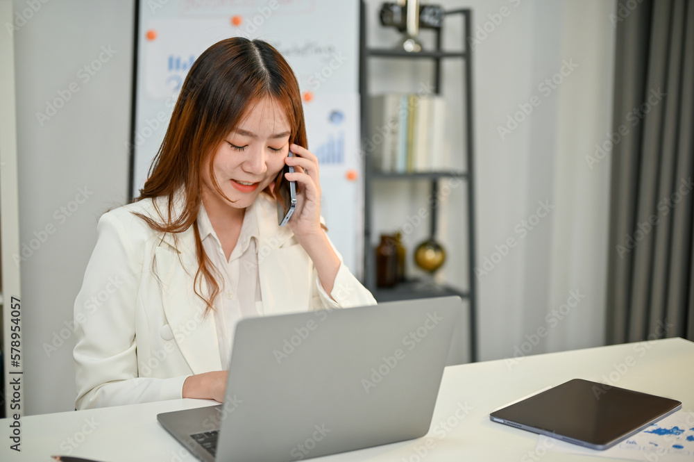 Attractive Asian businesswoman is talking on the phone with her business client Attractive Asian businesswoman is talking on the phone with her business client