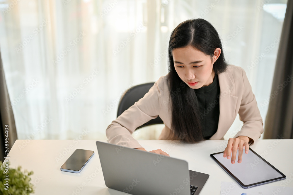 Professional millennial Asian businesswoman focusing on her business tasks on laptop Professional millennial Asian businesswoman focusing on her business tasks on laptop