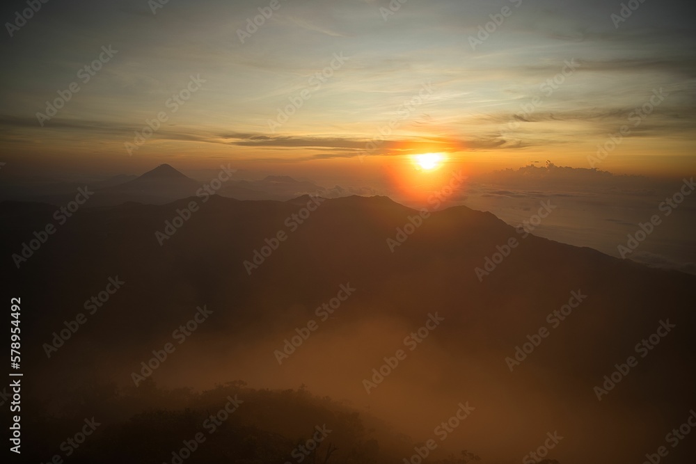 Obraz premium Epic sunrise on the top of the mountain Inerie on Flores, the sun bathes a sea of clouds in red yellow golden colors, in the foreground hills.