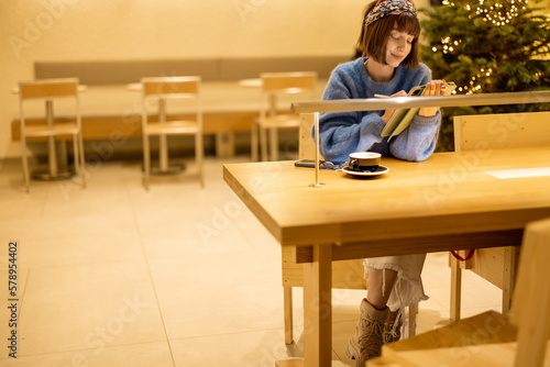 Young adult woman works on a digital tablet while sitting at modern coffee shop in yellow tones. Concept of remote creative work online