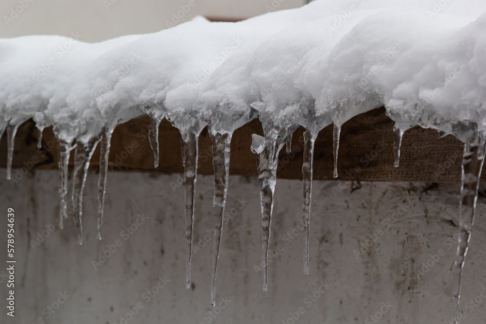 Sharp icicles and melted snow hanging from eaves of roof. Beautiful transparent icicles slowly gliding of a roof Sharp icicles and melted snow hanging from eaves of roof. Beautiful transparent icicles slowly gliding of a roof