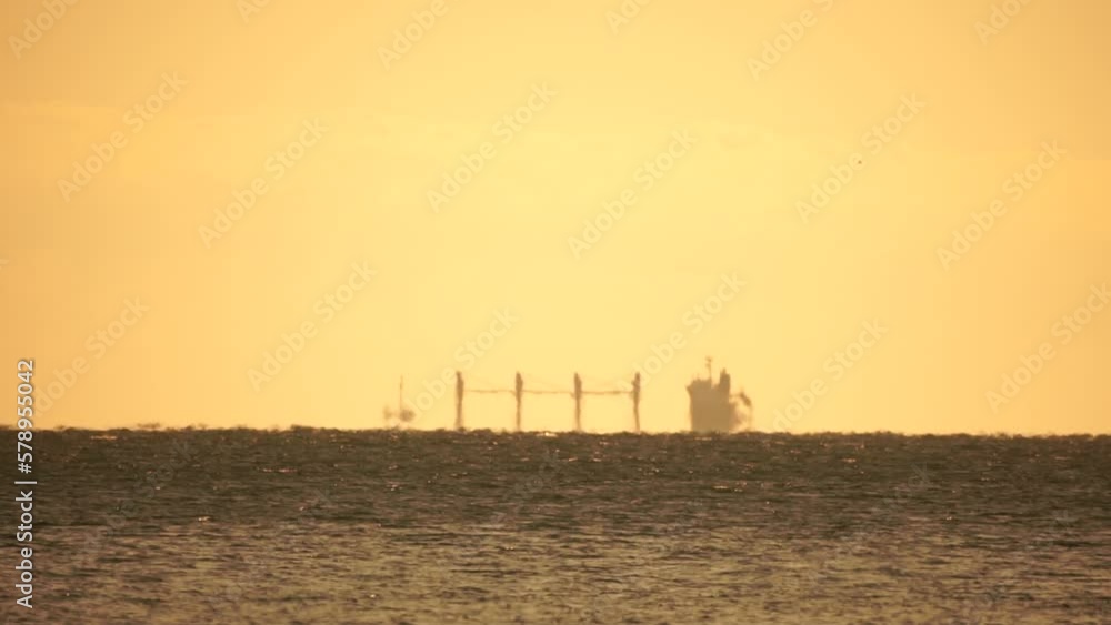 Mirage of cargo ship in the sea beyond the horizon. Ship sailing in the sea. Small waves on the golden surface of warm water with bokeh lights from the sun. Sea, nature and outdoor travel. Mirage of cargo ship in the sea beyond the horizon. Ship sailing in the sea. Small waves on the golden surface of warm water with bokeh lights from the sun. Sea, nature and outdoor travel.