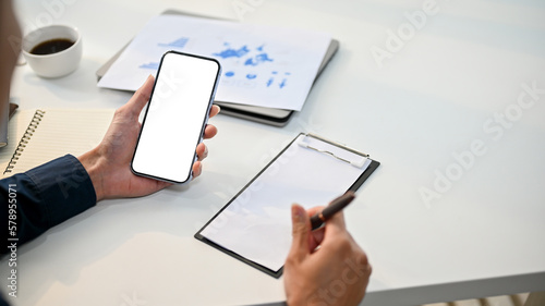 Professional millennial Asian businessman is using his phone and noting something on paper