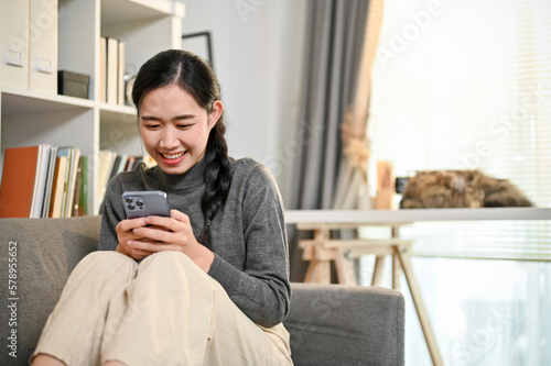Pretty Asian woman enjoys chatting with her friends on social media while chilling on sofa
