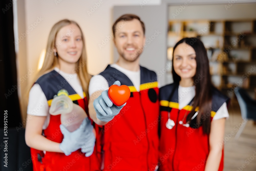 A group of young medical people in uniform stand in the middle of the classroom and smile after a first aid lesson. A man holds a red heart in his hands. Concept of assistance A group of young medical people in uniform stand in the middle of the classroom and smile after a first aid lesson. A man holds a red heart in his hands. Concept of assistance