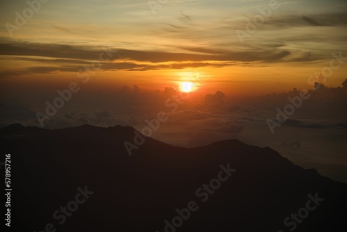 Epic sunrise on the top of the mountain Inerie on Flores, the sun bathes a sea of clouds in red yellow golden colors, in the foreground hills. © Monika