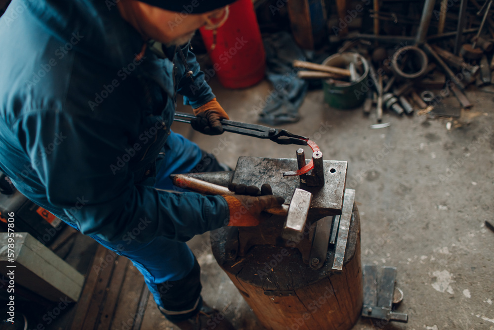 Blacksmith forges and makes metal horseshoe with hammer and anvil at forge.