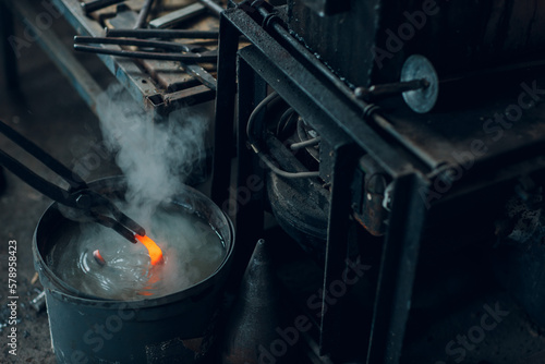 Papier peint Blacksmith forges and tempering metal horseshoe in jar with water at forge