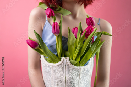 Happy girl in silk blouse with flowers tulips in hands on a pink background.