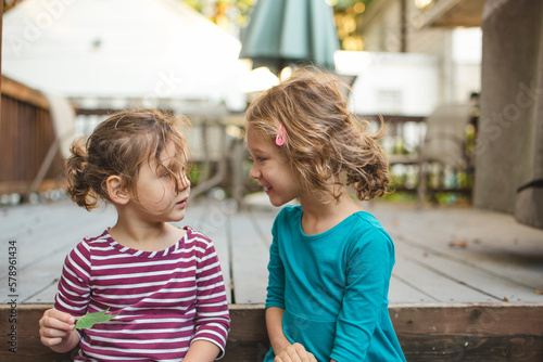 two little girls sit happily on a deck in conversation