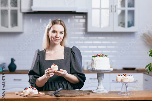 Pastry chef confectioner young caucasian woman holds cupcake in hands cake on kitchen table. Cakes cupcakes and sweet dessert photo