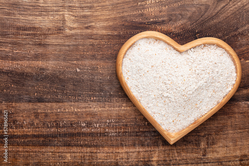 Wheat flour in a wooden heart shape bowl on a pastel background.