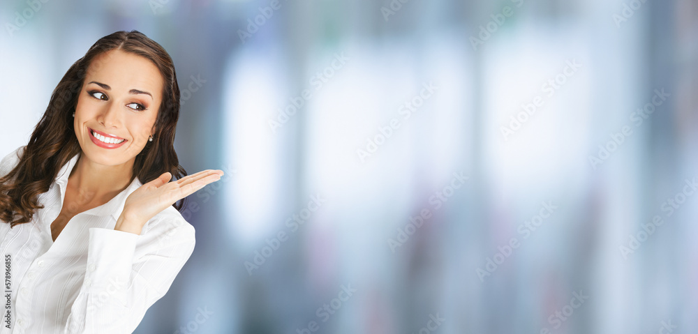 Happy smiling woman in confident blouse giving, holding, showing, advertising some product or copy space. Business advertisement concept. Brunette businesswoman on blurred office interior background. Happy smiling woman in confident blouse giving, holding, showing, advertising some product or copy space. Business advertisement concept. Brunette businesswoman on blurred office interior background.
