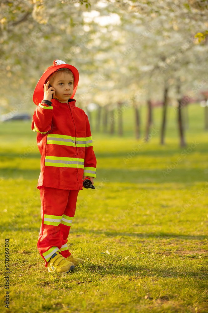Little toddler child with fireman costume in park, pretending to be real fireman, playing Little toddler child with fireman costume in park, pretending to be real fireman, playing