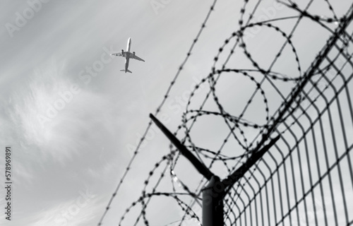 Airplane silhouette in the background. Barbed wire fence detail. Black and white.