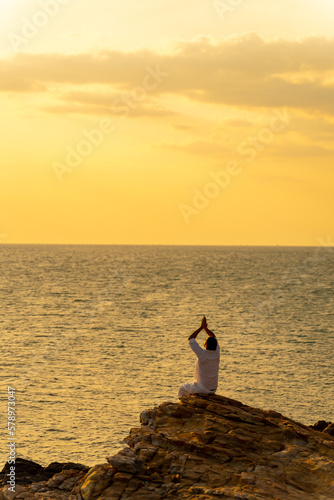 Caucasian man practicing meditation prayer with ocean nature on rocky coastal hill at summer sunset. Wellness people do outdoor self relaxing yoga exercise. Mental health care and motivation concept. © CandyRetriever 