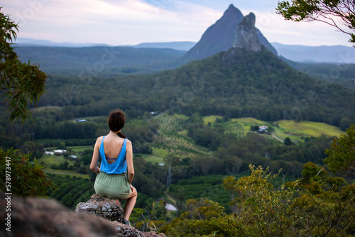 Beautiful girl sits on top of the Ngungun Mountain and admires the Beerwah and Coonowrin mountains in Glass House National Park, Queensland, Australia photo