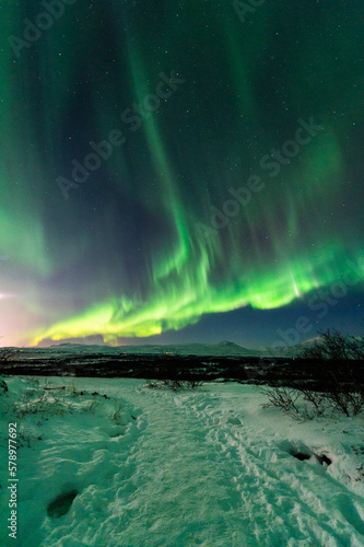 imagen de un paisaje nocturno nevado  con monta  as de fondo  y una aurora boreal sobre el cielo de Islandia 