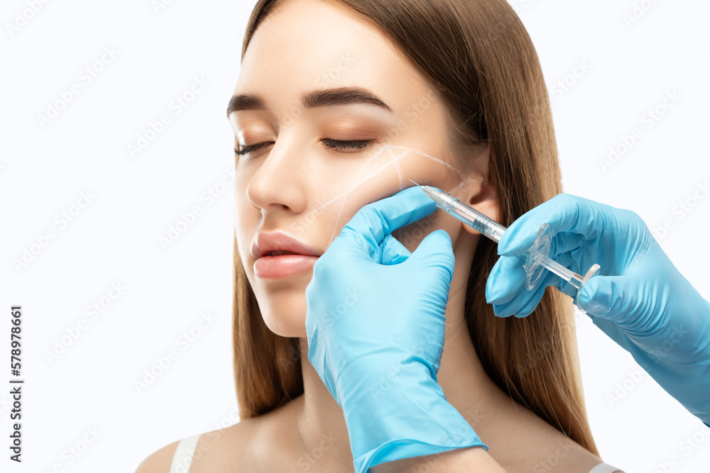 © Dimid - The cosmetologist makes injections of the cheekbones of a beautiful woman. Women's cosmetology in a beauty salon.