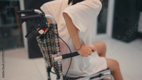 A paralyzed woman is trying to stand up from her wheelchair with an expression of pain