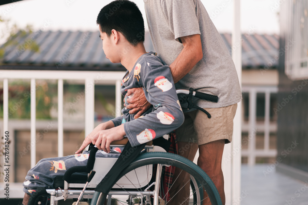 Obraz premium Young man with disability on wheelchair and father or volunteer or caregiver at happy time in the house, Caring for love and positive energy from parents, mental health, Family Caregiving concept.