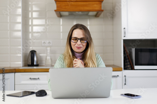 Pleased online teacher learning students on video call. Cheerful white woman in glasses looking at computer screen with a smile