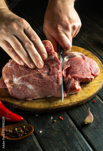 Cook's hands cut a raw beef steak with a knife on a wooden cutting board. The concept of process of preparing a meat dish for lunch with aromatic spices