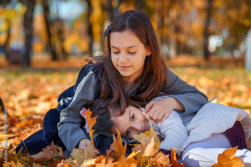 two girls are sitting in a glade of yellow maple leaves in an autumn city park, children are playing and enjoying, picking leaves near a tree, beautiful nature, bright sunny day two girls are sitting in a glade of yellow maple leaves in an autumn city park, children are playing and enjoying, picking leaves near a tree, beautiful nature, bright sunny day