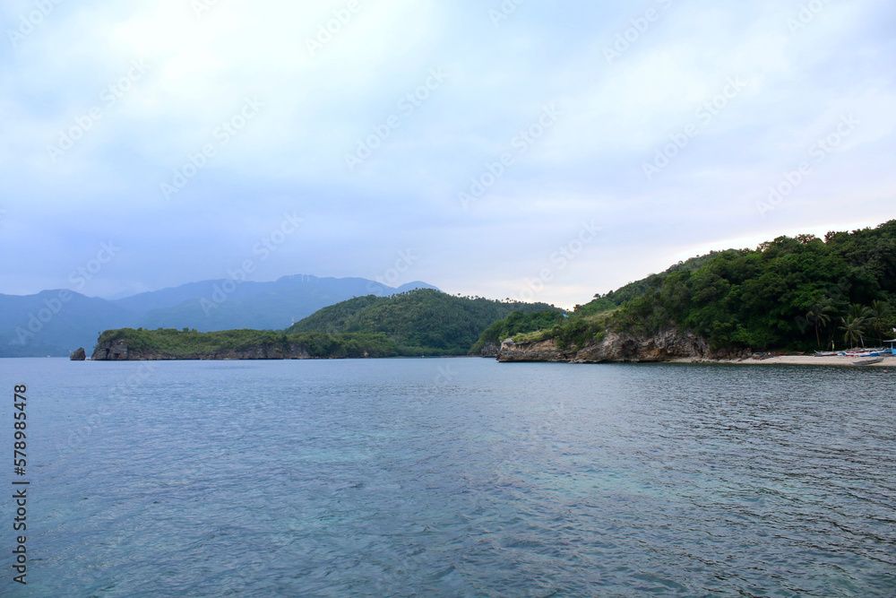 View of a hilly tropical island and a calm sea. View of a hilly tropical island and a calm sea.