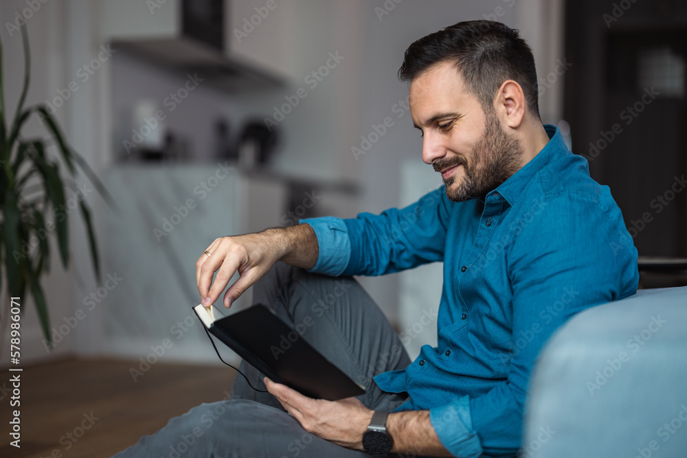 Fototapeta premium Businessman reading a book, taking a work break, sitting at the home office.