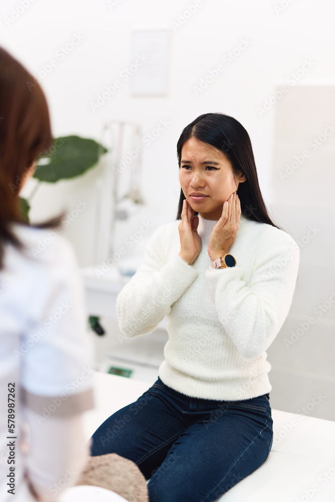 An adult Asian female patient talking with a female doctor about head pain. An adult Asian female patient talking with a female doctor about head pain.