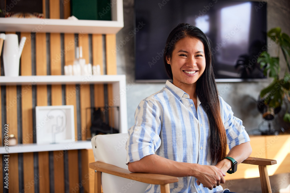 Portrait of a smiling Asian woman, sitting on an armchair, enjoying herself.