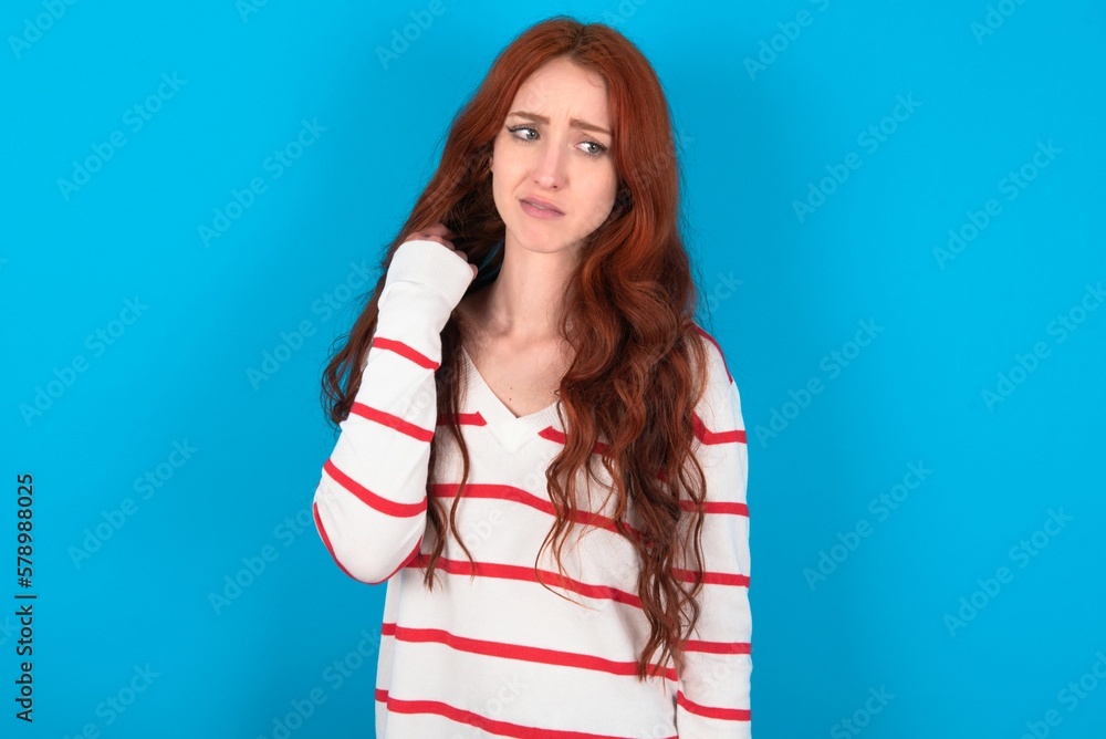 young woman wearing striped sweater over blue background stressed, anxious, tired and frustrated, pulling shirt neck, looking frustrated with problem young woman wearing striped sweater over blue background stressed, anxious, tired and frustrated, pulling shirt neck, looking frustrated with problem
