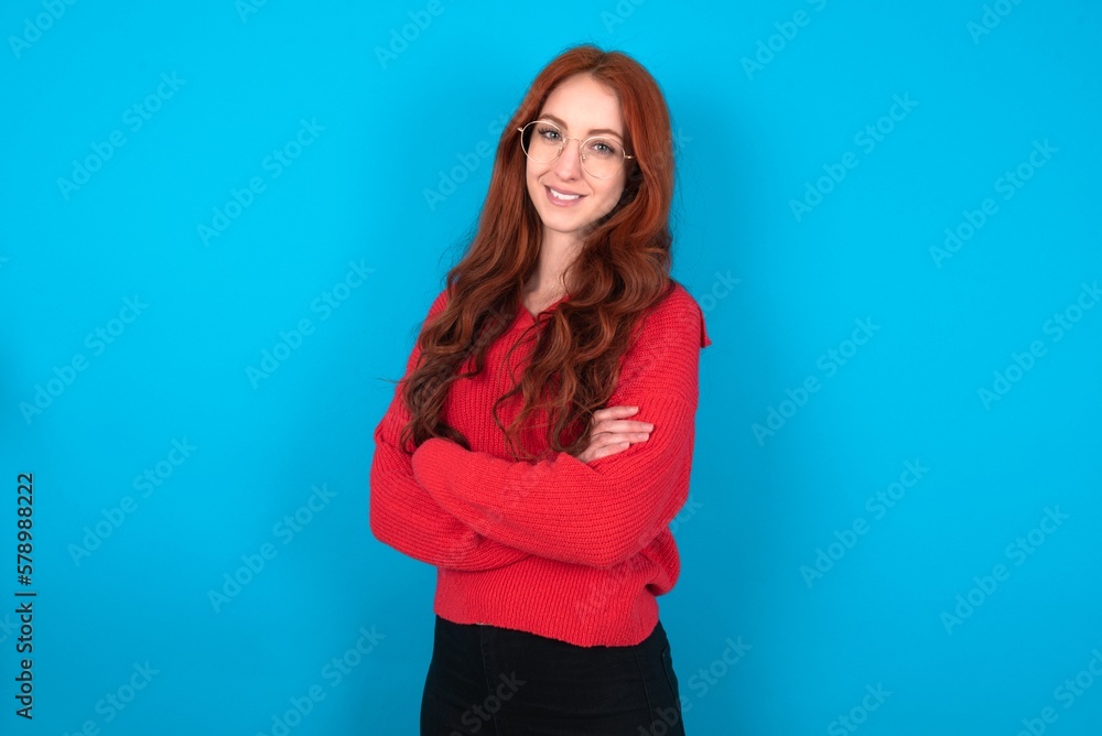 Portrait of young woman wearing red sweater over blue background standing with folded arms and smiling Portrait of young woman wearing red sweater over blue background standing with folded arms and smiling