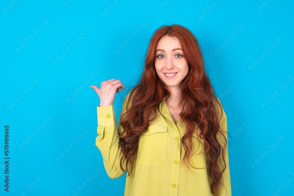 Lovely young woman wearing green sweater over blue background pointing aside with forefinger, showing at copy space having news about bargains Lovely young woman wearing green sweater over blue background pointing aside with forefinger, showing at copy space having news about bargains
