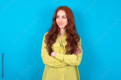 Dreamy rest relaxed young woman wearing green sweater over blue background crossing arms, looks good copyspace