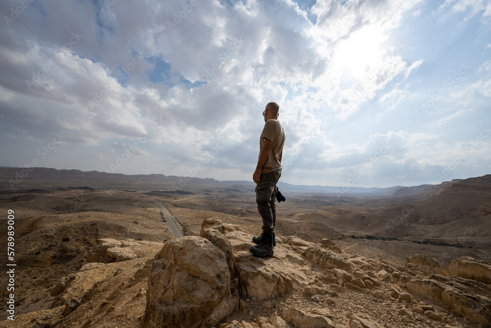 A man is standing on the edge of a cliff and looking down at the valley in rhe Negev desert in Israel.