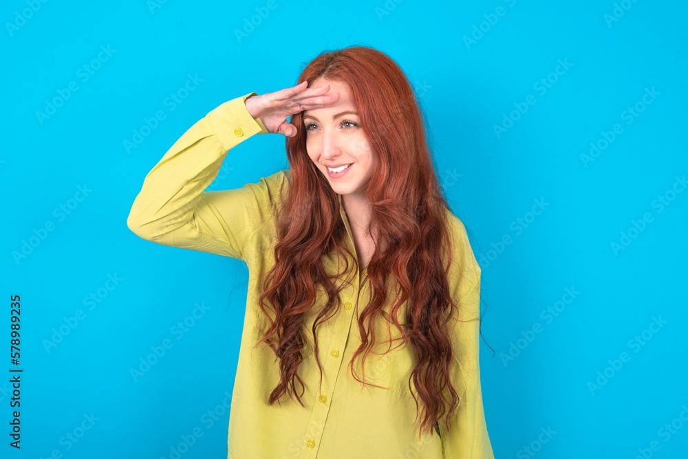 young woman wearing green sweater over blue background very happy and smiling looking far away with hand over head. Searching concept. young woman wearing green sweater over blue background very happy and smiling looking far away with hand over head. Searching concept.