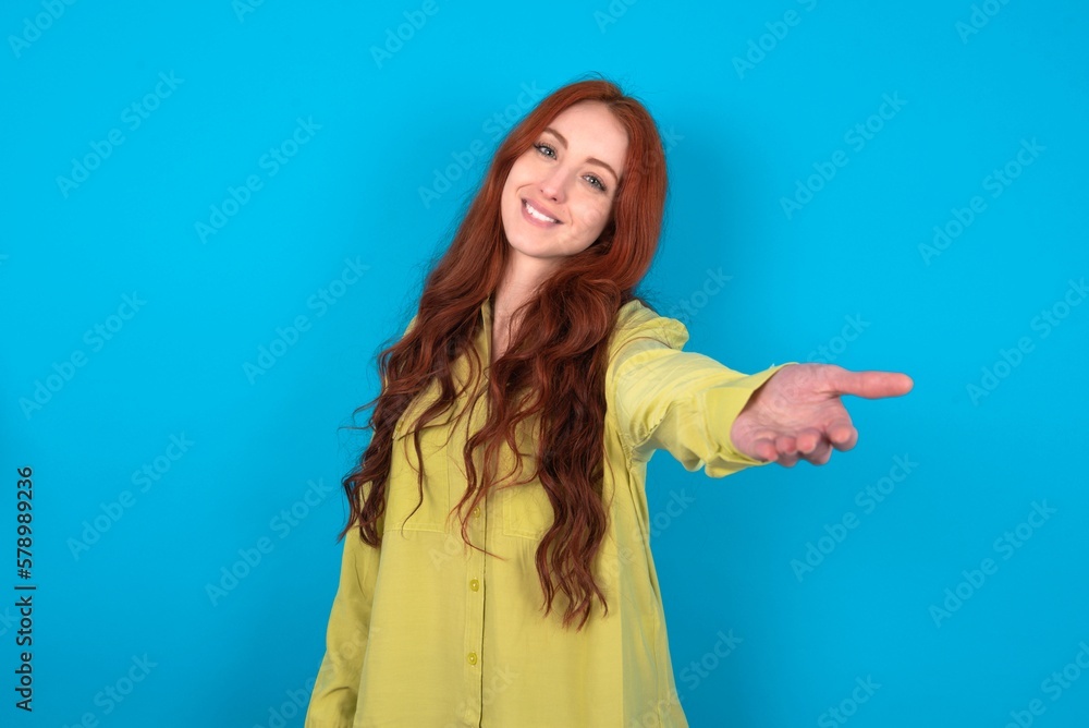 young woman wearing green sweater over blue background smiling friendly offering handshake as greeting and welcoming. Successful business. young woman wearing green sweater over blue background smiling friendly offering handshake as greeting and welcoming. Successful business.
