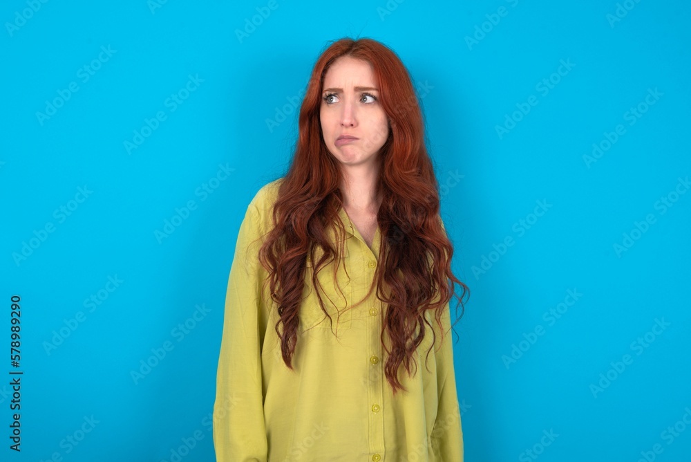 young woman wearing green sweater over blue background making grimace and crazy face, screaming out of control, funny lunatic expressing freedom and wild. young woman wearing green sweater over blue background making grimace and crazy face, screaming out of control, funny lunatic expressing freedom and wild.