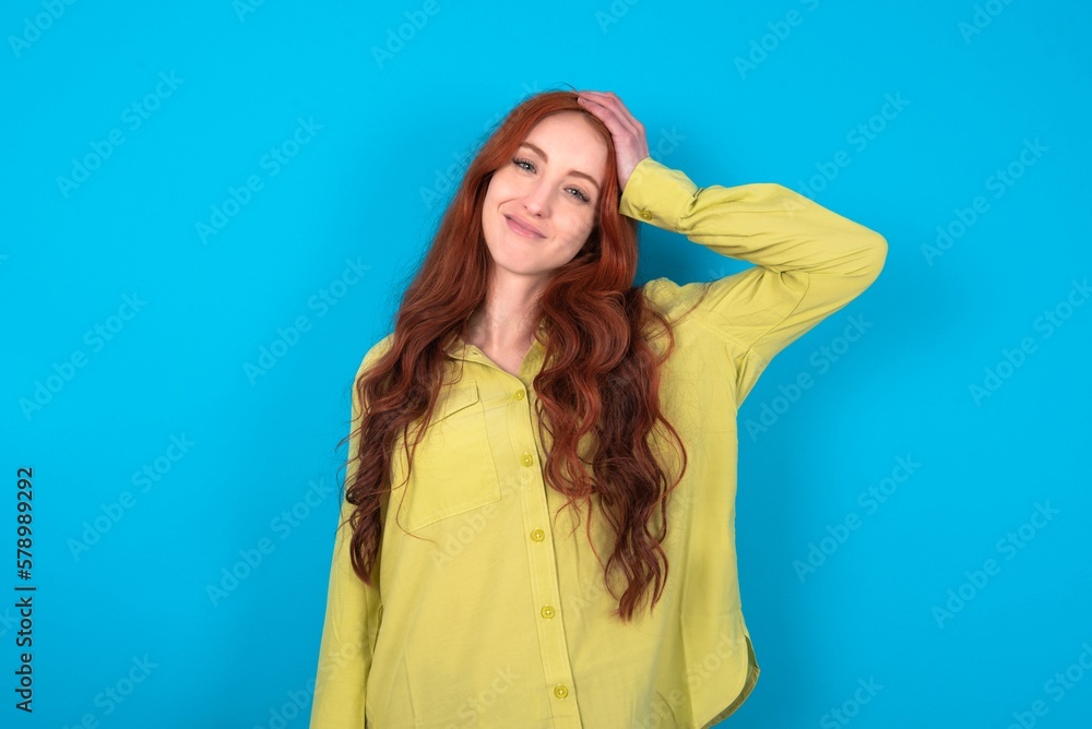 young woman wearing green sweater over blue background being confused and wonders about something. Holding hand on head, uncertain with doubt. Pensive concept. young woman wearing green sweater over blue background being confused and wonders about something. Holding hand on head, uncertain with doubt. Pensive concept.