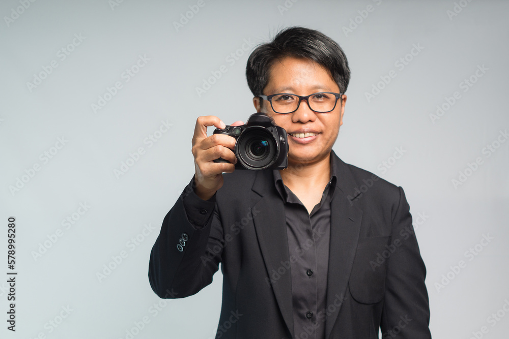 Photographer in a suit holding the digital camera while standing on a gray background Photographer in a suit holding the digital camera while standing on a gray background