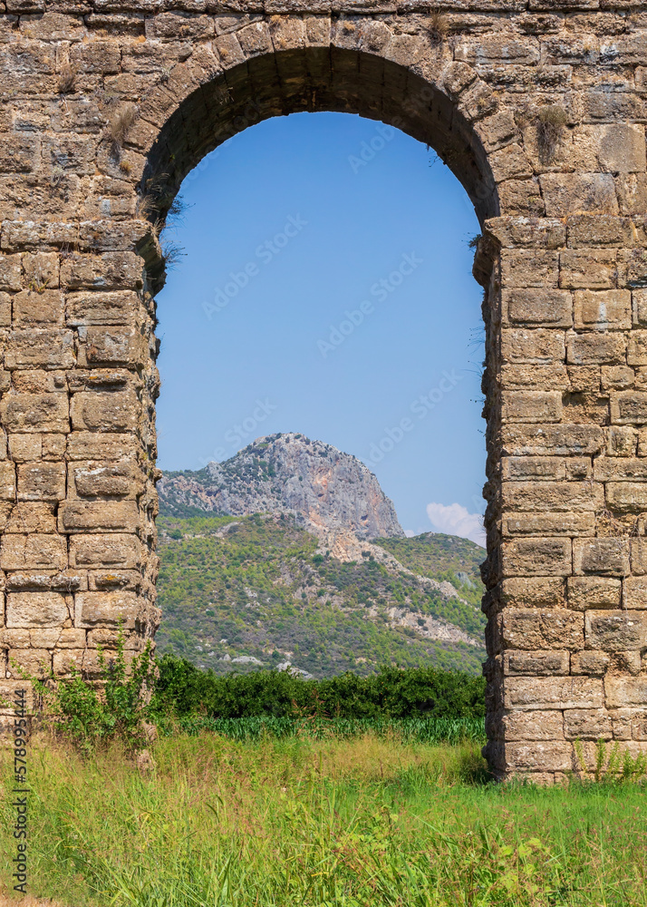 Mountain as seen through the aqueduct arch. Roman aqueduct at Aspendos, part of water supply ancient system. Vertical shot. Antalya region, Turkey (Turkiye). History and archaeology background