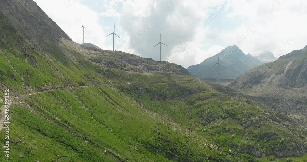 Grimsel Pass Mountain Road With Wind Turbines At Background In Bernese Alps, Switzerland. Aerial Drone Shot Grimsel Pass Mountain Road With Wind Turbines At Background In Bernese Alps, Switzerland. Aerial Drone Shot