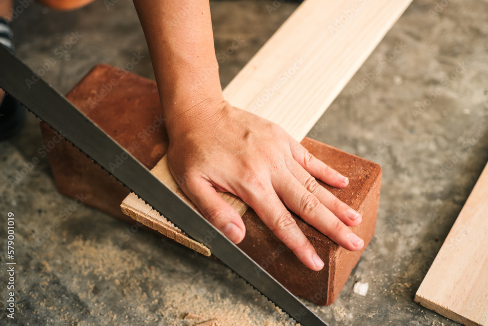 Close up carpenter craftsman using hand saw in workshop. Small business furniture industry.