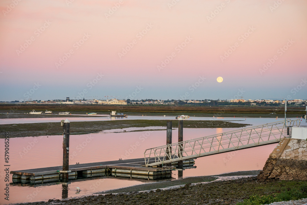 Morning view of pier on Ria Formosa in Faro, with moon set shortly before sun rise, Algarve, Portugal